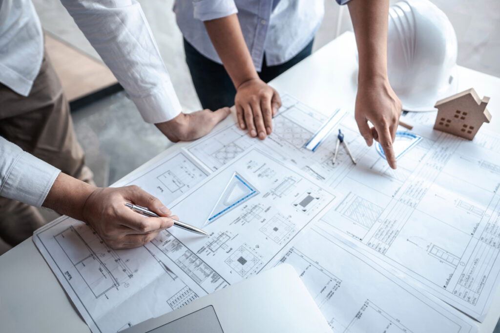 Team of architects or engineering consulting and analyzing working on objects tools and construction drawings inspection, discussing planning new architectural project on blueprint and model house.